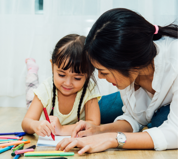 Young girl practicing drawing with her mother laying beside her.