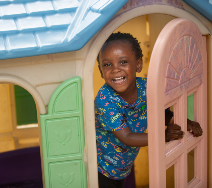 Young boy smiling while looking out the door of a colorful playhouse.