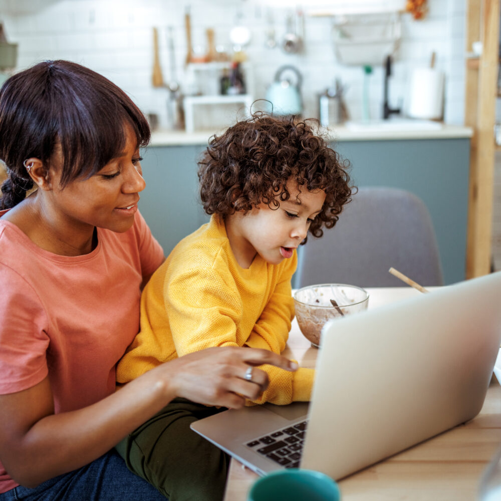 Mother and cute little boy using laptop while having breakfast together at home